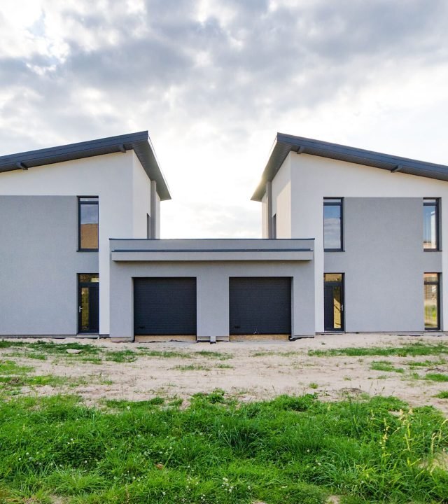 Front view of twin modern houses with a symmetrical architectural design under a cloudy sky.